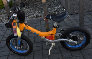 pomarańczowy rowerek biegowy stojący na chodniku