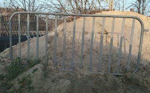 metalowa barierka drogowa, w tle pryzma piachu i ogrodzenie